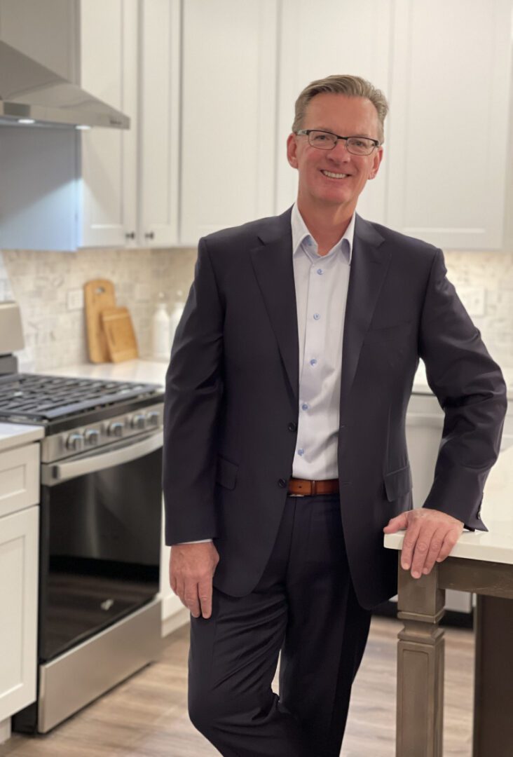 A man in a suit standing in a kitchen.